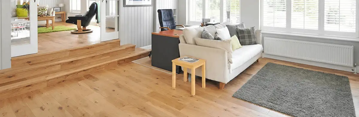 A modern living room with professionally installed laminate flooring, a beige sofa, a small side table, a gray rug, and large windows with white shutters in Sacramento, CA